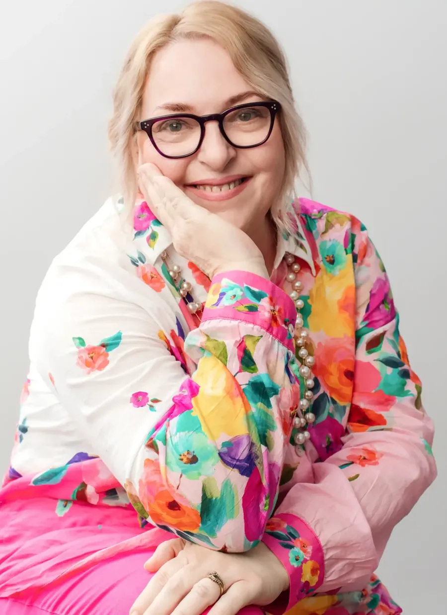 Marianne Edwards smiling, resting her chin on her hand, in glasses and a bright floral shirt