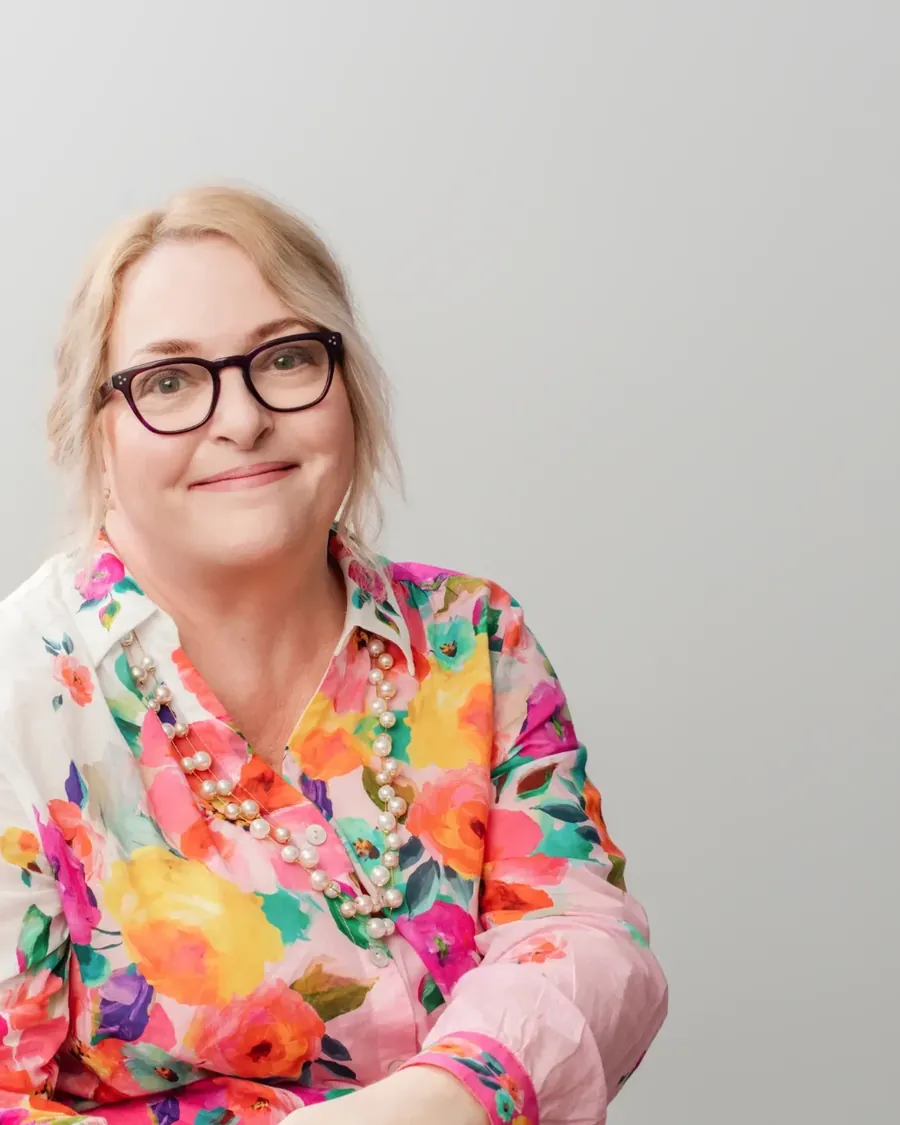 Marianne Edwards sitting and smiling, in a bright floral shirt and pearls